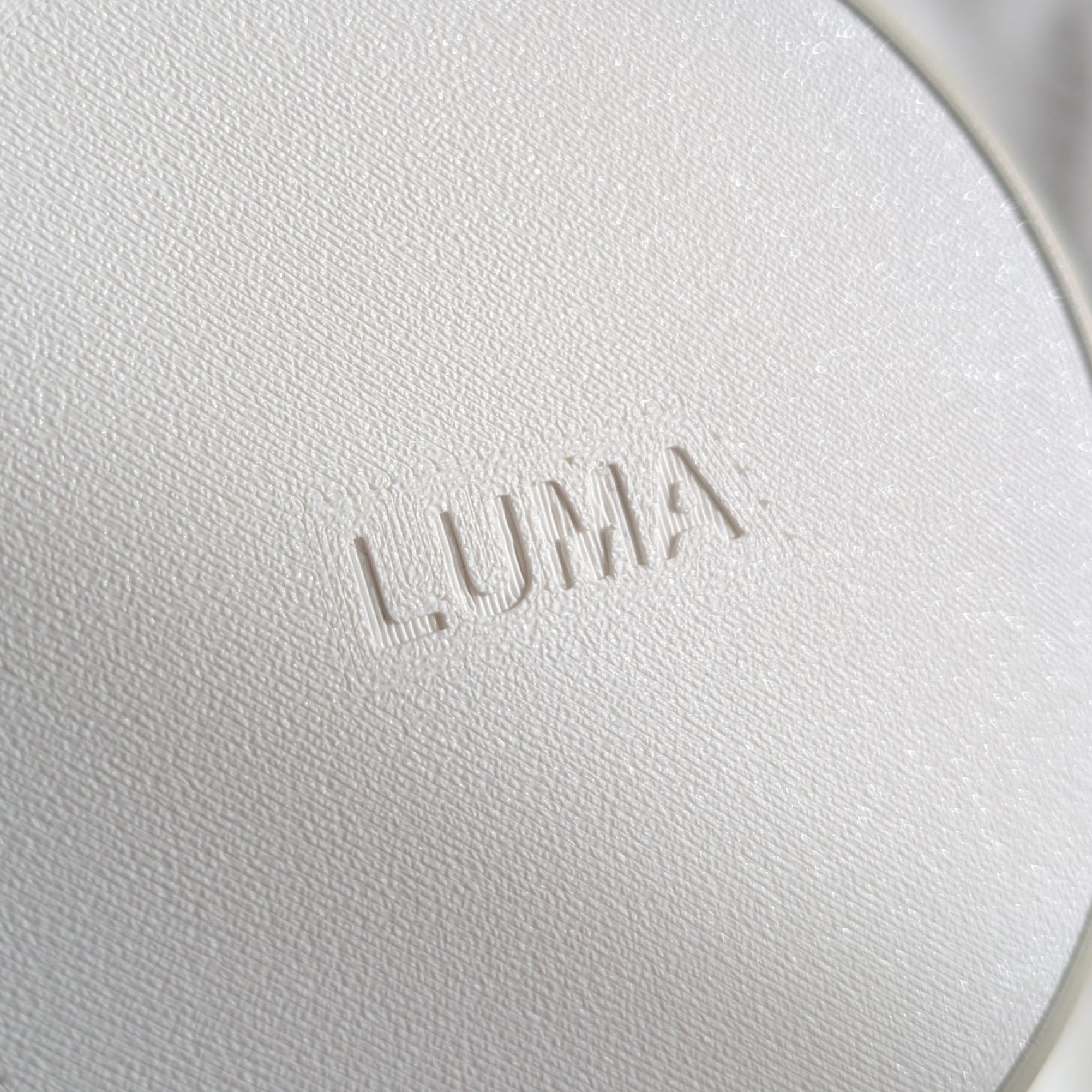 Round white device with 'LUMA' branding held by a hand against a neutral background