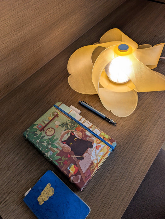 HANA in Sunset Yellow lit on a wooden desk beside books