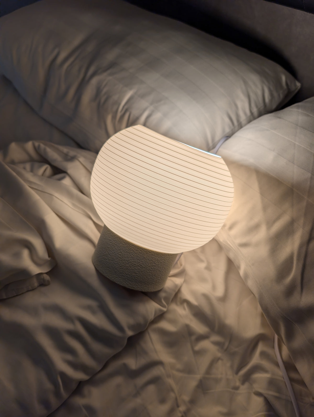 KAMI lamp lit warm on a bed at night